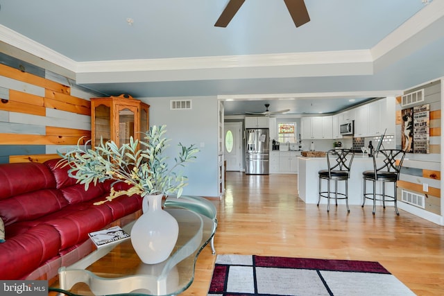 living room with visible vents, ornamental molding, light wood-style flooring, and ceiling fan