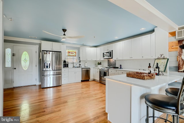 kitchen featuring ceiling fan, white cabinets, a peninsula, ornamental molding, and stainless steel appliances
