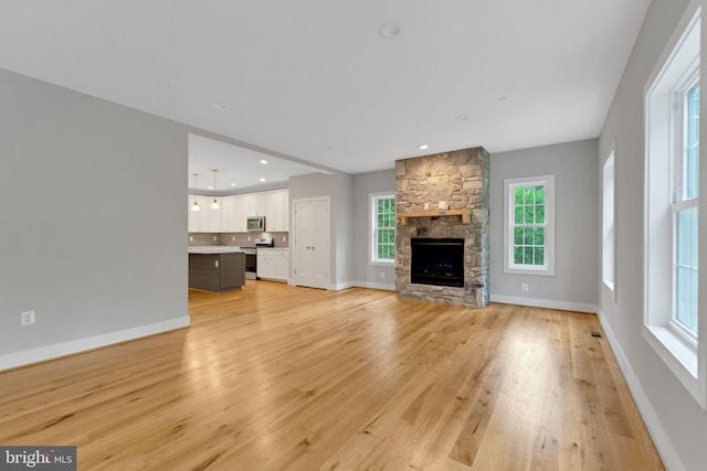 unfurnished living room featuring baseboards, light wood-style flooring, a wealth of natural light, and a fireplace
