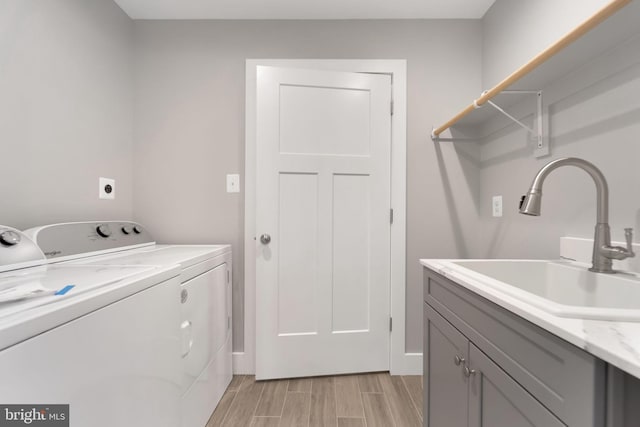 washroom featuring wood tiled floor, washing machine and clothes dryer, cabinet space, a sink, and baseboards