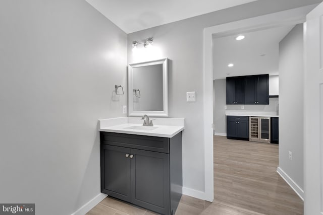 bathroom with vanity, wood finished floors, beverage cooler, baseboards, and recessed lighting
