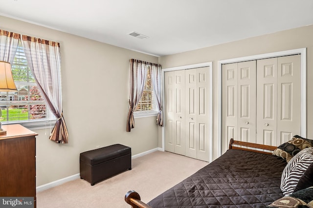carpeted bedroom featuring baseboards, multiple windows, two closets, and visible vents
