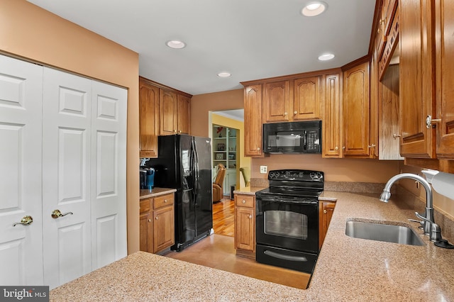 kitchen featuring light stone counters, a sink, brown cabinetry, recessed lighting, and black appliances
