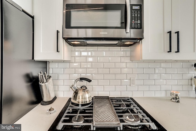kitchen with decorative backsplash, white cabinetry, stainless steel microwave, and black gas stovetop