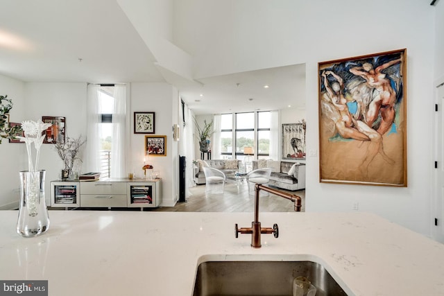 kitchen featuring open floor plan, light stone counters, a sink, and wood finished floors