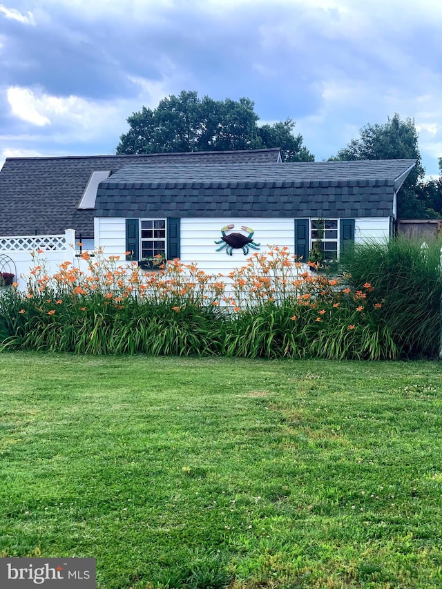 exterior space with a shingled roof and a front lawn