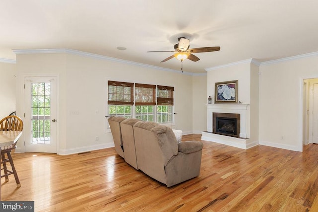 living area featuring crown molding, a ceiling fan, light wood finished floors, and a tile fireplace
