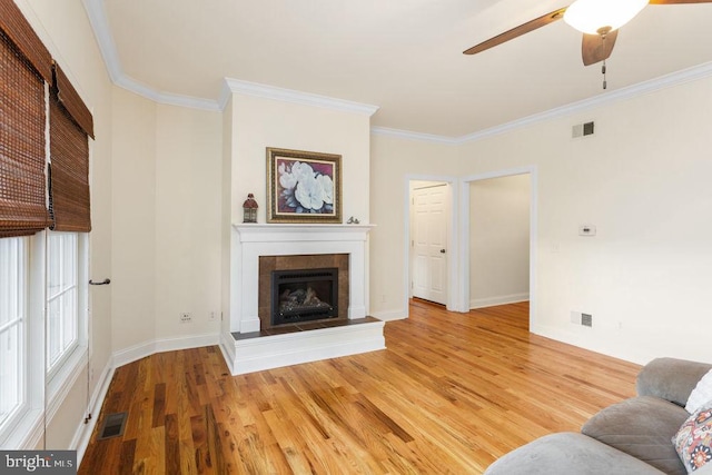living room with crown molding, ceiling fan, light wood finished floors, a tile fireplace, and visible vents