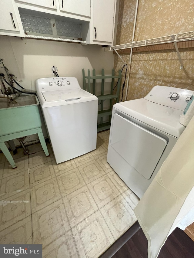 laundry room featuring washing machine and clothes dryer, a sink, light floors, and cabinet space