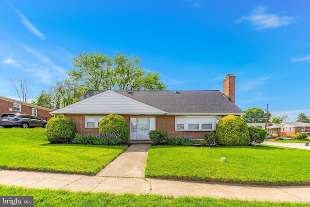bungalow featuring brick siding, roof with shingles, a chimney, and a front yard