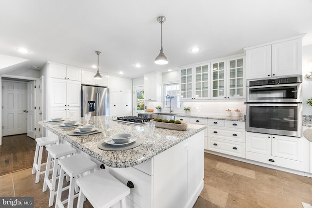 kitchen featuring glass insert cabinets, white cabinets, light stone counters, a sink, and appliances with stainless steel finishes