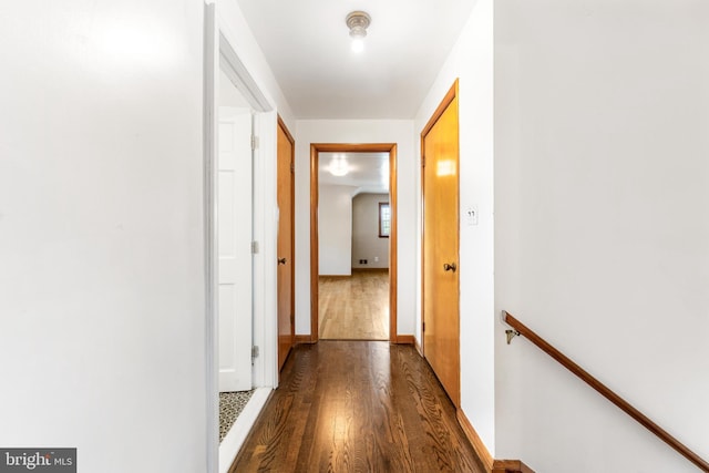 hallway featuring baseboards, dark wood-style flooring, and an upstairs landing