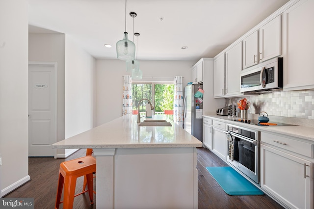 kitchen with appliances with stainless steel finishes, a sink, white cabinetry, decorative backsplash, and dark wood-style floors
