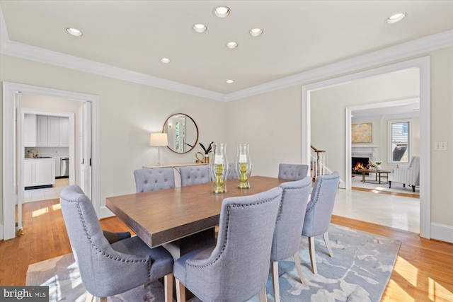 dining space with recessed lighting, ornamental molding, light wood finished floors, and a warm lit fireplace