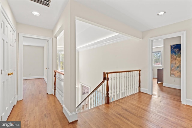 hallway featuring visible vents, baseboards, recessed lighting, light wood-type flooring, and an upstairs landing