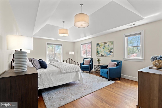 bedroom featuring light wood-style floors, a raised ceiling, baseboards, and visible vents
