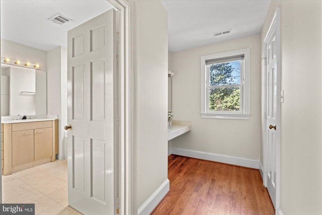 hall with baseboards, visible vents, a sink, and light wood-style flooring