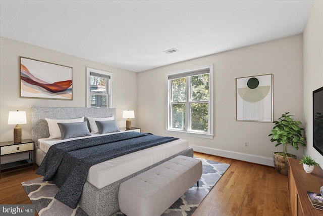 bedroom with baseboards, multiple windows, wood finished floors, and visible vents