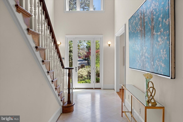 tiled foyer featuring stairway, baseboards, and a high ceiling
