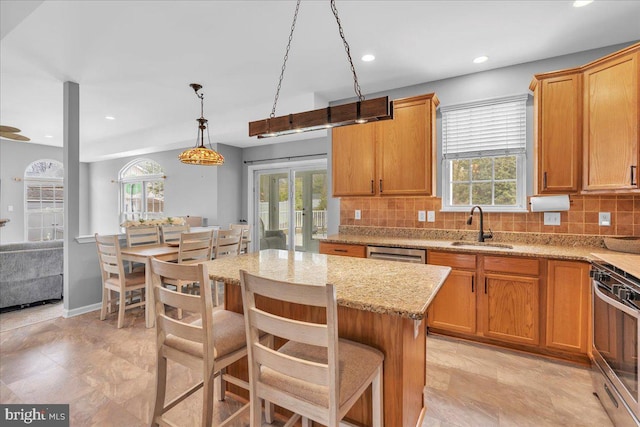 kitchen featuring light stone counters, decorative backsplash, a sink, and a wealth of natural light