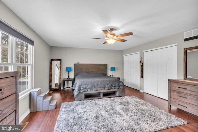 bedroom featuring ceiling fan, multiple closets, baseboards, wood finished floors, and visible vents