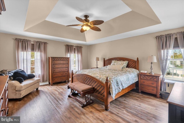 bedroom with a tray ceiling, ceiling fan, and light wood finished floors