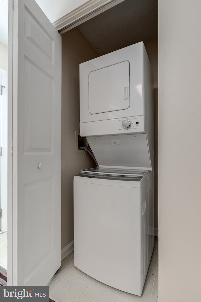 laundry room featuring light tile patterned floors, baseboards, laundry area, and stacked washer and dryer