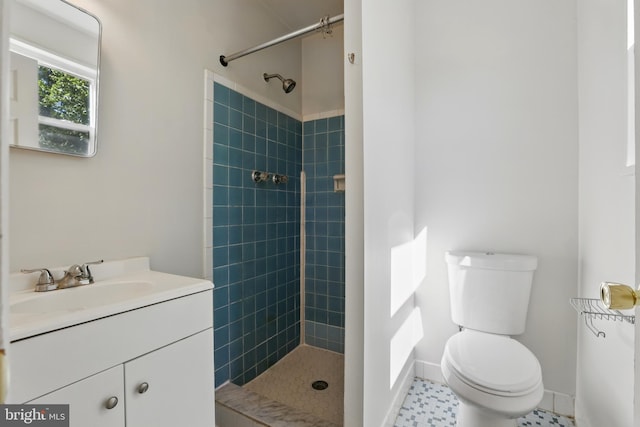 bathroom with toilet, a tile shower, vanity, and baseboards