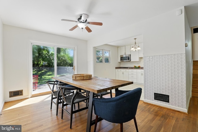 dining room featuring light wood-type flooring, ceiling fan, a chandelier, and baseboards