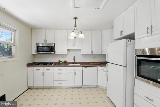 kitchen with stainless steel appliances, a sink, dark countertops, and white cabinetry