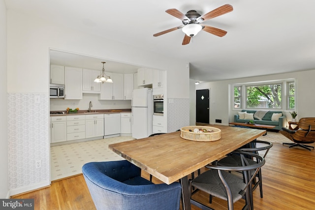 dining space with light wood finished floors, a ceiling fan, a chandelier, and baseboards