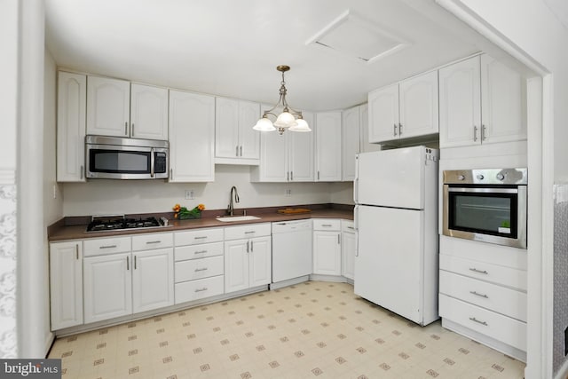 kitchen with stainless steel appliances, a sink, dark countertops, white cabinetry, and light floors