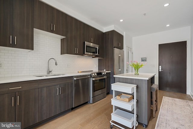 kitchen with light wood-type flooring, light countertops, a sink, appliances with stainless steel finishes, and backsplash
