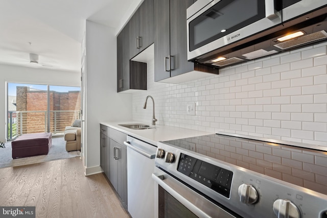 kitchen with decorative backsplash, light wood-type flooring, a sink, light countertops, and stainless steel appliances