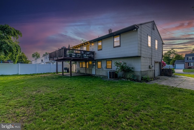 back of house at dusk with a deck, an attached garage, concrete driveway, and central AC unit