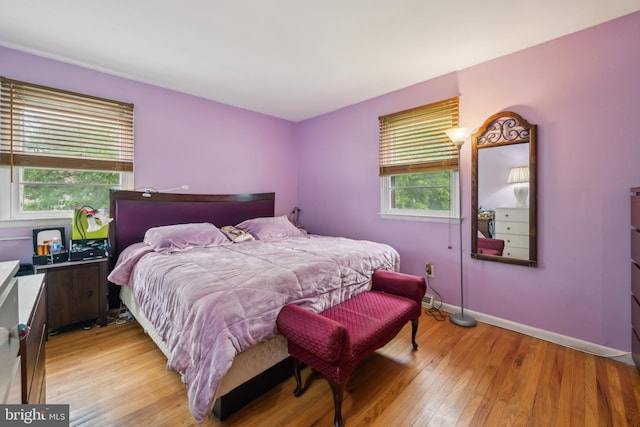 bedroom with multiple windows, light wood finished floors, and baseboards