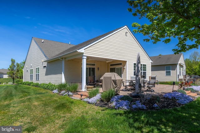 rear view of property featuring a lawn, a patio, and roof with shingles