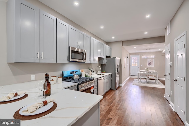 kitchen featuring wood finished floors, light stone countertops, recessed lighting, a sink, and appliances with stainless steel finishes