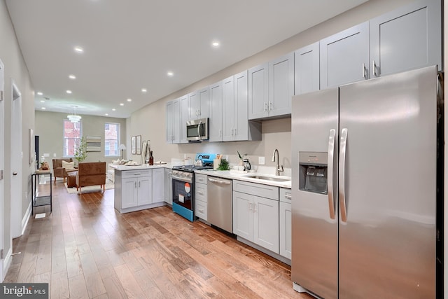 kitchen featuring a peninsula, light wood-type flooring, light countertops, a sink, and stainless steel appliances