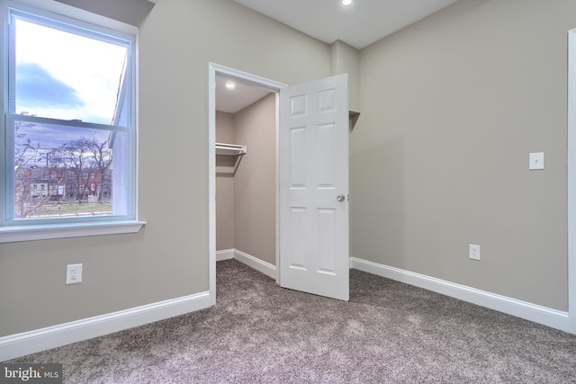 unfurnished bedroom featuring carpet floors, baseboards, a spacious closet, and multiple windows