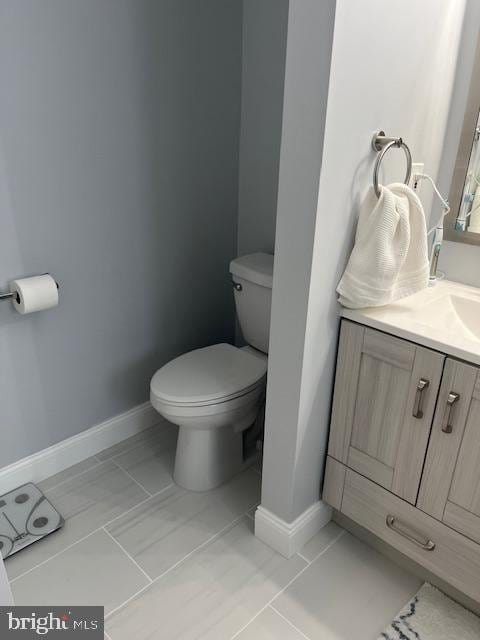 bathroom featuring toilet, baseboards, marble finish floor, and vanity