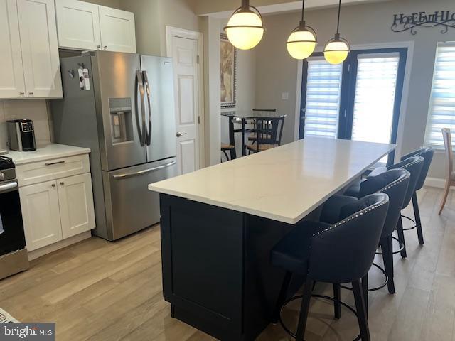 kitchen with appliances with stainless steel finishes, white cabinets, a kitchen island, and light wood finished floors