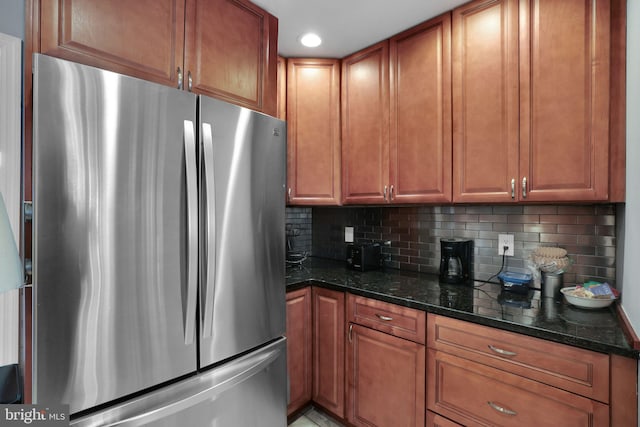 kitchen with freestanding refrigerator, backsplash, brown cabinets, and dark stone counters