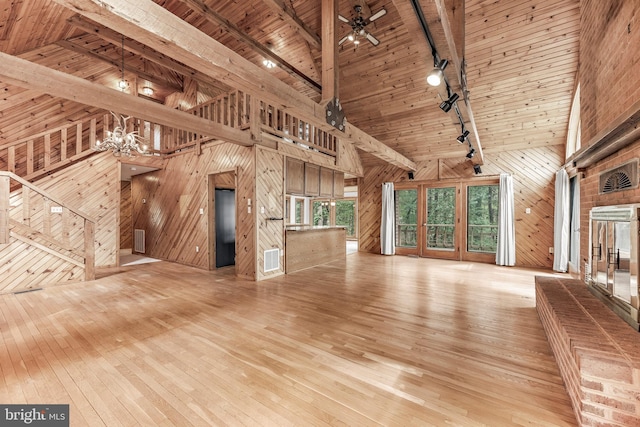 unfurnished living room with track lighting, wooden walls, high vaulted ceiling, wood ceiling, and light wood-style flooring