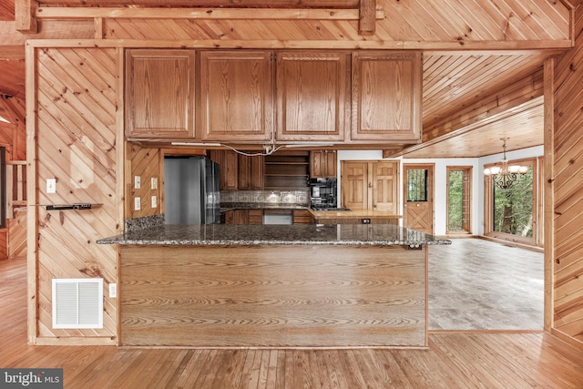 kitchen featuring wood walls, light wood-style flooring, dark stone countertops, freestanding refrigerator, and visible vents