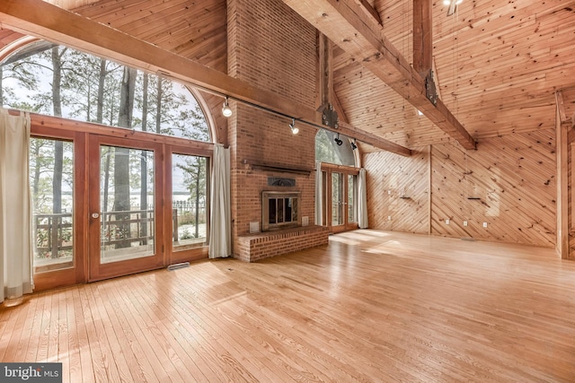 unfurnished living room with wood-type flooring, wood walls, track lighting, beam ceiling, and high vaulted ceiling