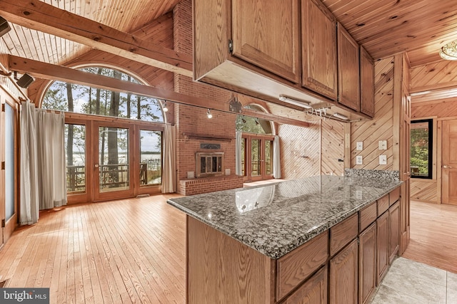 kitchen with light wood-type flooring, wood walls, wood ceiling, and dark stone counters