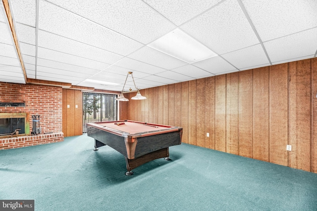 game room featuring carpet flooring, wooden walls, a brick fireplace, pool table, and a drop ceiling