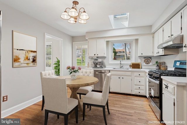 kitchen featuring light countertops, under cabinet range hood, a sink, appliances with stainless steel finishes, and a skylight
