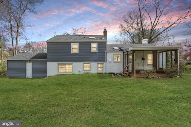 rear view of property featuring a sunroom, a lawn, and a chimney